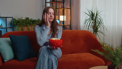 Mujer-Sentada-En-El-Sofá-Comiendo-Palomitas-De-Maíz-Y-Viendo-Interesantes-Series-De-Televisión,-Juegos-Deportivos-En-Línea-En-Casa