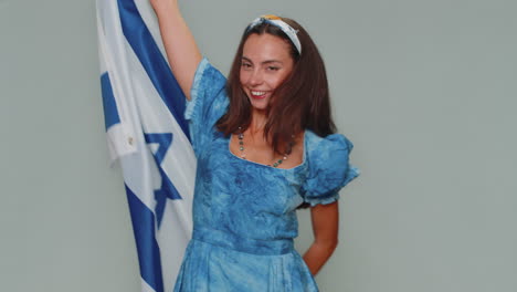 Mujer-Joven-Con-Vestido-Azul-Ondeando-Y-Envolviendo-La-Bandera-Nacional-De-Israel,-Celebrando-El-Día-De-La-Independencia