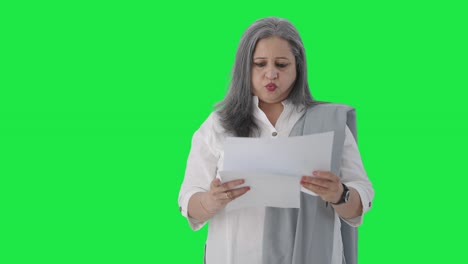 Confused-Indian-senior-female-manager-reading-business-reports-Green-screen