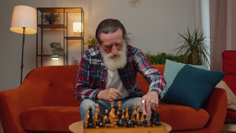 Focused-senior-grandfather-man-playing-chess-leisure-board-game-alone,-domestic-activity-at-home