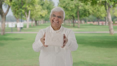 Happy-Indian-old-man-giving-a-gift-in-park