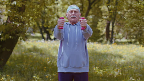 Hombre-Mayor-Haciendo-Ejercicio,-Haciendo-Ejercicios-De-Levantamiento-De-Pesas-Con-Mancuernas,-Practicando-Entrenamiento-Deportivo-En-El-Parque