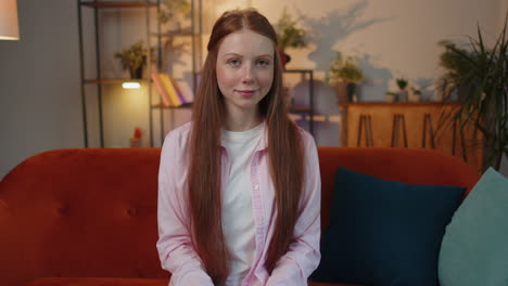 Close-up-of-happy-beautiful-young-redhead-child-girl-smiling-looking-at-camera-at-home-on-couch