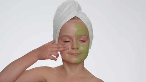 Beautiful-smiling-child-girl-kid-in-towel-on-head-applying-cleansing-moisturizing-green-facial-mask