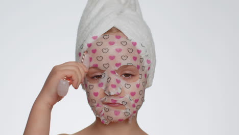 Beautiful-young-smiling-child-girl-applying-cosmetic-moisturizing-face-mask,-use-massage-roller