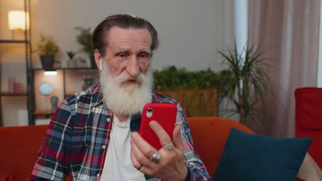 Senior-grandfather-man-making-phone-conversation-call-with-family-sitting-on-couch-at-home-in-room