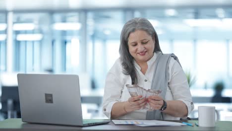 Cheerful-Indian-senior-businesswoman-counting-money