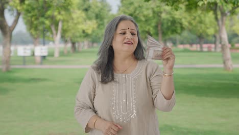 Happy-Indian-old-woman-using-money-as-fan-in-park