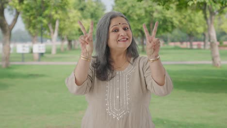 Happy-Indian-old-woman-showing-victory-sign-in-park