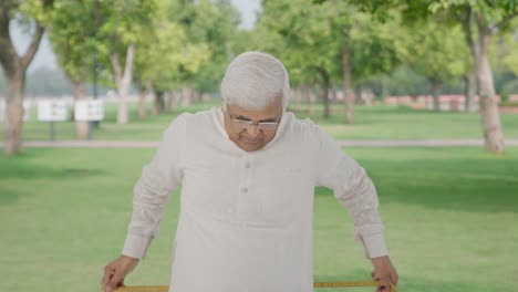 Sad-Indian-old-man-measuring-waist-using-inch-tape-in-park