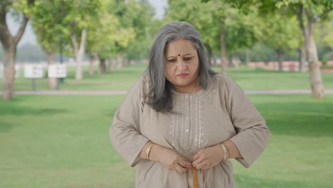 Sad-Indian-old-woman-measuring-waist-using-inch-tape-in-park