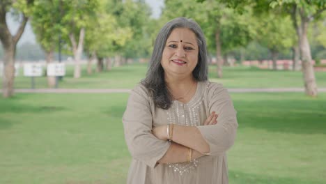 Happy-Indian-old-woman-standing-crossed-hands-in-park