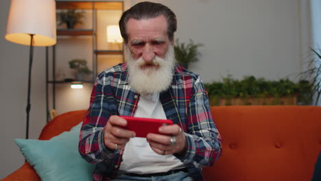 Worried-funny-senior-old-grandfather-man-playing-racing-online-video-games-on-smartphone-at-home