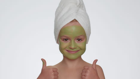 Beautiful-smiling-child-girl-kid-in-towel-on-head-applying-cleansing-moisturizing-green-mask-on-face