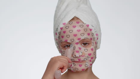 Beautiful-young-smiling-child-girl-applying-cosmetic-moisturizing-face-mask,-use-massage-roller