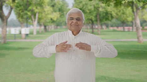 Relaxed-Indian-old-man-doing-breathe-in-breathe-out-exercise-in-park