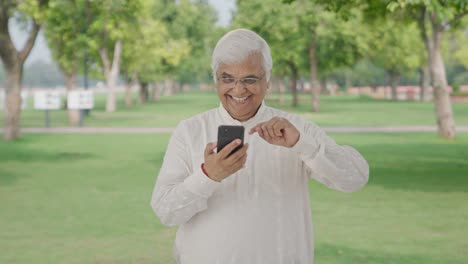 Happy-Indian-old-man-scrolling-through-phone-in-park