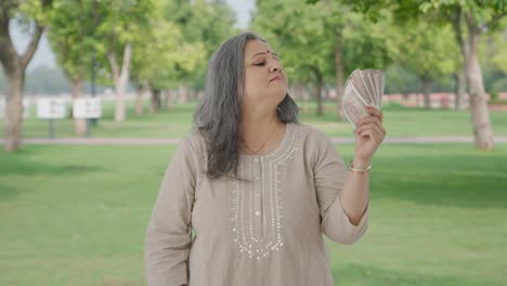 Confident-Indian-old-woman-using-money-as-fan-in-park