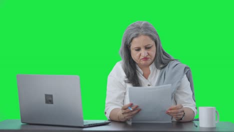 Tensed-Indian-senior-female-manager-reading-business-reports-Green-screen