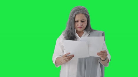 Indian-senior-female-manager-reading-business-reports-Green-screen