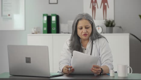 Happy-Indian-senior-female-doctor-reading-medical-reports