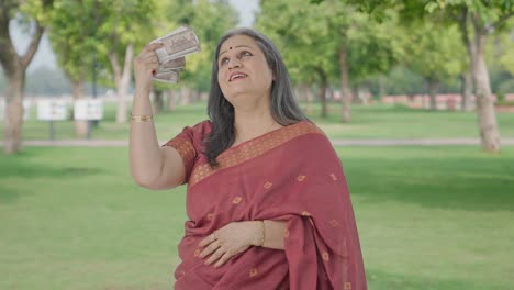 Cheerful-Indian-old-woman-using-money-as-fan-in-park