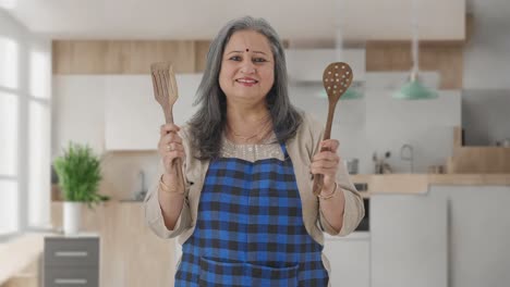 Happy-Indian-aged-housewife-posing-with-spoon-and-spatula