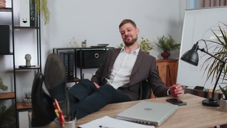 Businessman-drinking-champagne-from-glass-after-working,-putting-legs-on-table-sitting-at-office