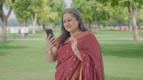 Happy-Indian-old-woman-scrolling-through-phone-in-park