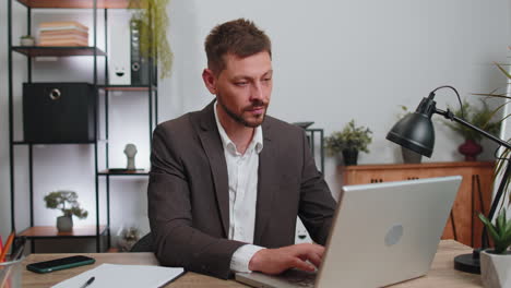 Businessman-working-on-office-laptop-pointing-to-camera-looking-with-happy-expression-making-choice