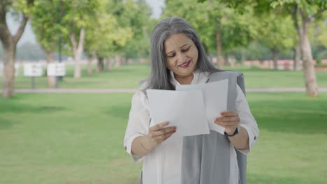 Glückliche-Alte-Indische-Frau-Liest-Berichte-Im-Park