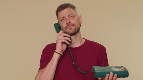 Crazy-man-in-red-t-shirt-talking-on-wired-vintage-telephone-of-80s,-fooling-making-silly-faces