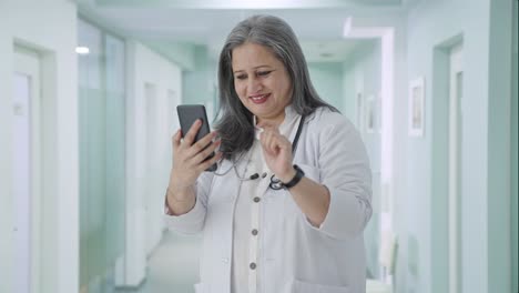 Happy-Indian-senior-female-doctor-scrolling-phone