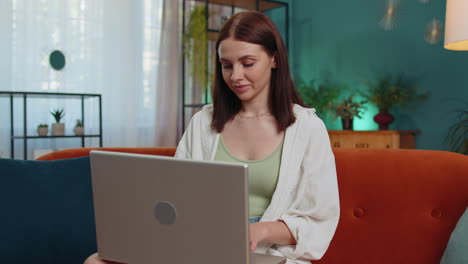 Young-woman-freelancer-sitting-on-sofa-closing-laptop-pc-after-finishing-work-in-living-room-at-home