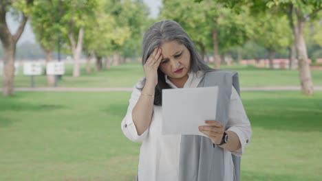 Stressed-Old-indian-woman-reading-reports-in-park