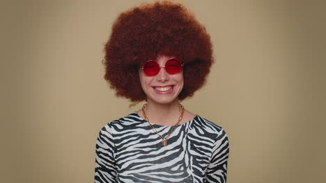 Cheerful-lovely-pretty-young-woman-with-brown-lush-wig-in-red-sunglasses-smiling,-looking-at-camera