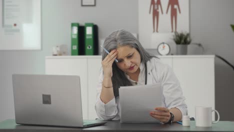 Stressed-Indian-senior-female-doctor-reading-medical-reports