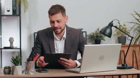 Businessman-working-with-documents-at-office-desk,-taking-a-break,-playing-smartphone-online-games