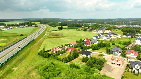 Luftaufnahme-Eines-Vorortviertels-Mit-Einer-Autobahn,-Die-Entlang-Grüner-Felder-Verläuft