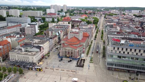 Drone-shot-of-Market-Square-in-Katowice,-a-cityscape-with-apartment-buildings,-tram-stops,-Silesian-Theatre-in-view