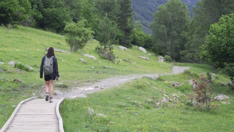 Girl-trekking-in-nature-with-a-backpack-in-a-green-mountainous-environment-on-a-trail