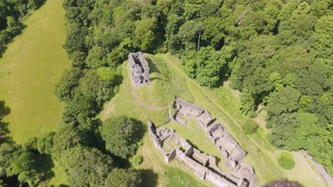 Drone-establishment-shot-of-Okehampton-Castle-amidst-dense-greenery-in-Devon,-UK