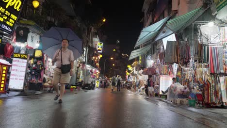 Night-vibes-on-street-after-rain-surrounded-by-shop-lights,-city-market