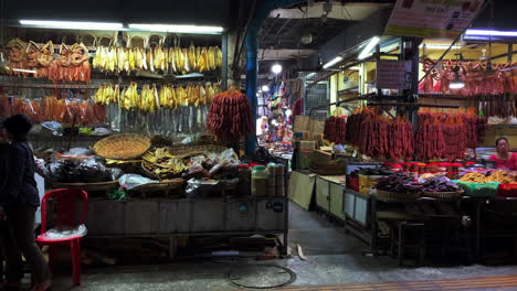 Cured-meats-hanging-in-Asian-night-market-with-swirling-fans,-wide-shot