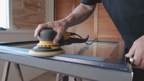 Older-adult-man-uses-sander-for-sanding-a-window-frame-for-painting