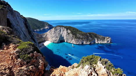 Impresionante-Vista-Aérea-Del-Mirador-De-La-Playa-De-Navagio,-Con-Acantilados-Blancos,-Aguas-Turquesas-Y-Barcos-Navegando-Por-El-Mar-Sereno-Y-Cristalino-De-Zakynthos,-Grecia.