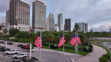 Amerikanische-Flaggen-Im-Bayfront-Park-Mit-Parkenden-Autos-Und-Der-Skyline-Der-Innenstadt-Im-Hintergrund