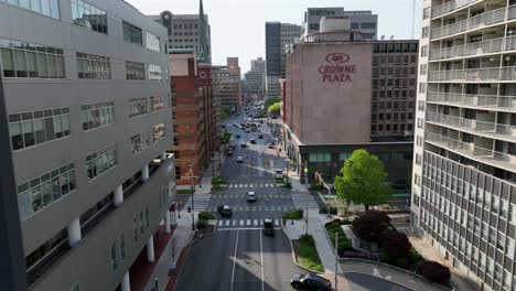 Drone-flight-over-main-street-of-american-town-with-crowne-plaza-buildings-and-traffic