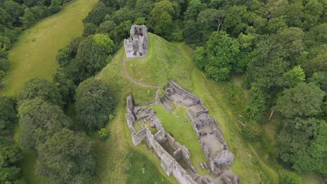 Aerial-fly-in-capturing-Okehampton-Castle-surrounded-by-dense-greenery-in-Devon,-UK