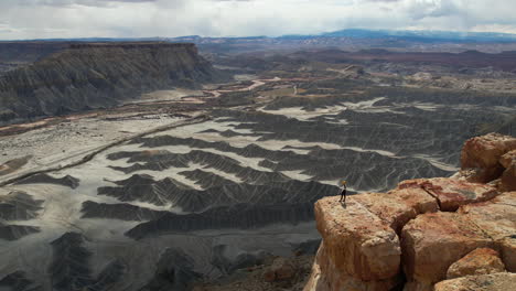 Toma-Aérea-De-Una-Mujer-Solitaria-Parada-En-El-Borde-De-Un-Acantilado-Sobre-Un-Cañón-Profundo-En-El-Desierto-De-Utah,-EE.-UU.